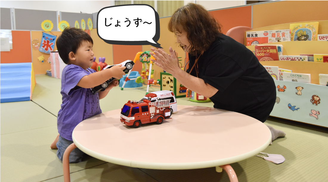 パトカーのおもちゃを見せる子どもと「じょうず～」と言っている先生の写真。