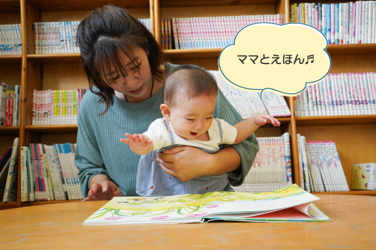 一緒に絵本を読んでいるお母さんと赤ちゃんの写真。赤ちゃんが「ママと絵本」と言っている。