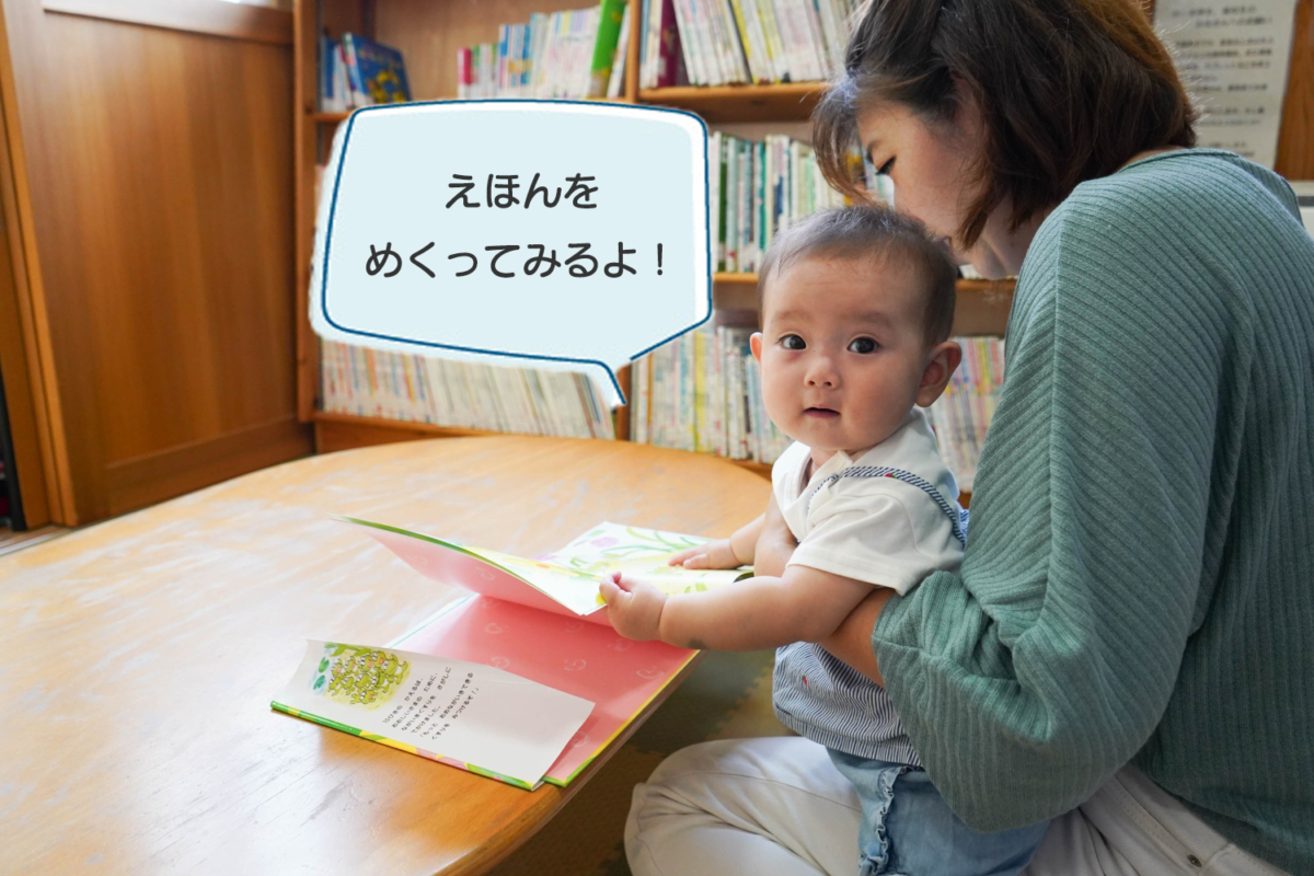 一緒に絵本を読んでいるお母さんと赤ちゃんの写真。赤ちゃんが「絵本をめくってみるよ」と言っている。
