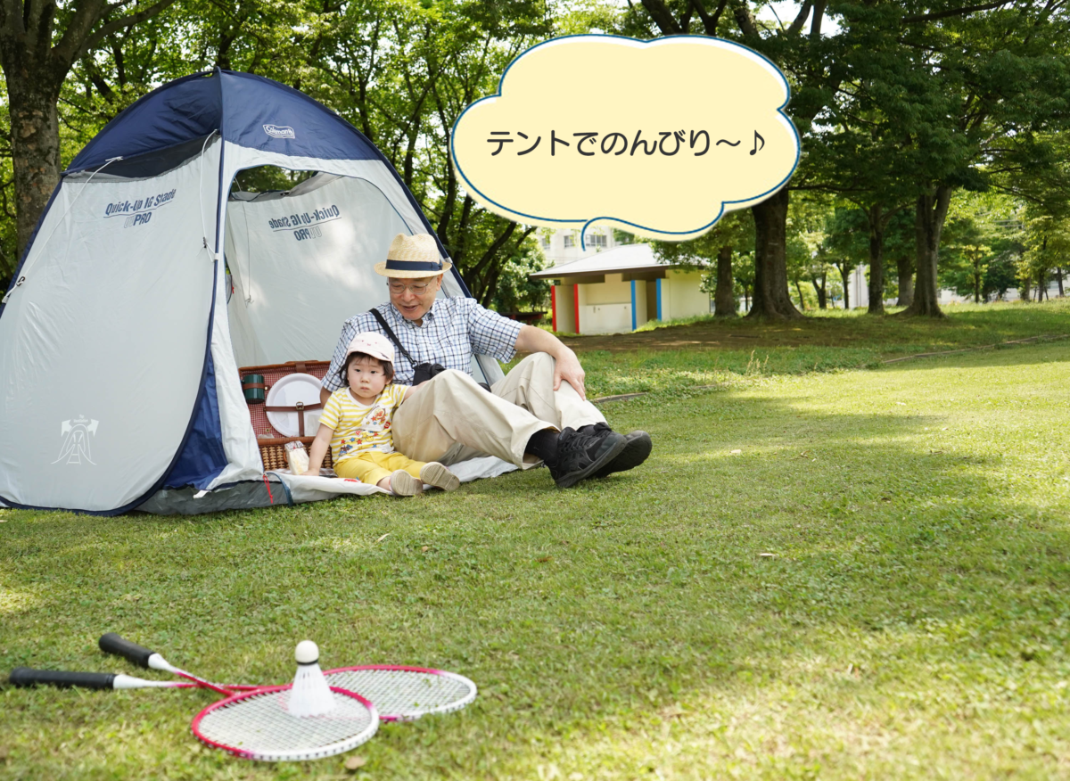 多目的スポーツ広場にテントを張り、テントの中で休んでいる子どもとおじいちゃんの写真。おじいちゃんが「テントでのんびり」と言っている。
