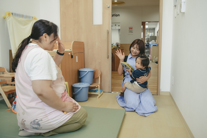 お迎えにきたママに抱っこされて、先生にバイバイしている写真